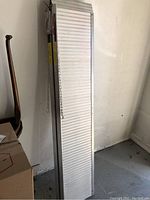 Pair of folded aluminum ramps standing upright against a wall, showing ribbed surface and chains.