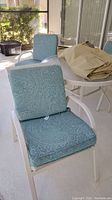 Four chairs around a patio table with blue paisley cushions; two swivel with circular bases and two stationary models with armrests. Beige fabric covers also visible.