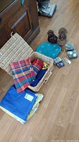 Overview showing wicker picnic basket filled with colorful tablecloths and napkin rings, plus blue placemat and decorations nearby on the floor