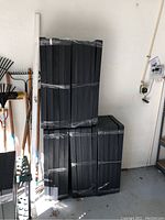 Five new sealed black plastic garage shelves stacked vertically, wrapped in plastic and tape.