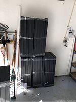 Five sealed, shrink-wrapped stackable black plastic shelving units stacked vertically, each unit with five shelves approximately 36 in by 18 in size.