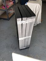 Four black plastic stackable shelves wrapped together, showing top and sides in sealed condition.