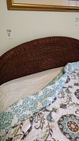 Curved rattan headboard attached to the bed frame with partial view of bedding on mattress.