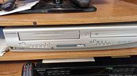 Front view of the silver Sylvania VHS and DVD combo unit showing the VHS tape slot, DVD drive, and control buttons.