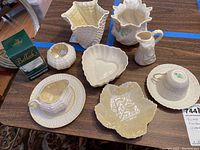 Full lot overview on table showing all 11 pieces of vintage Belleek Irish china including cups, saucers, dishes, vases, and a creamer.