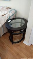 Side view of wood side table near bed, showing top glass beveled shelf and part of lower beveled glass shelf with wood frame.