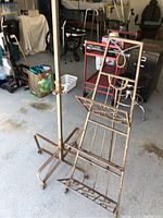 Image showing the wrought iron collapsible magazine rack with lattice angled support and base with casters, surface rust visible.