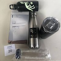 Top view photo showing the five beverage containers: black dinosaur skeleton stainless bottle, Trace Engineering stainless steel bottle, black tumbler with clear lid, new E-Flask in original box, and clear plastic bottle in plastic packaging.