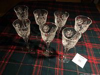 Seven clear crystal stemware glasses arranged on dark plaid cloth showing all glasses and their shapes.
