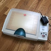 Agfa SnapScan Touch digital scanner closed with translucent lid, power adapter placed on top, photographed on wood floor.