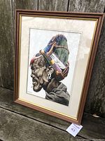 Full view of the framed painting showing the artwork within a wooden frame with gold accents and white matting, placed against an outdoor background.