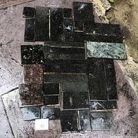 Multiple assorted granite pieces laid out on a wet surface showing varied sizes and colors including solid black and speckled green stones