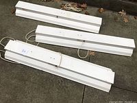 Three white metal grow-light fixtures arranged outdoors on the ground showing length and configuration