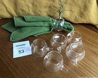 Six clear acrylic napkin rings arranged with one napkin visible, showing the stem opening with a sprig inserted.