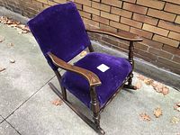 Front angled view of the vintage wooden rocking chair showing purple velvet seat and back upholstery, wooden armrests and rockers.