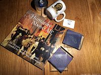 Four items on wooden floor: Toronto Star commemorative mug, wristwatch in round metal container with blue strap, 110th anniversary book 'Humanity Above All', and two square coasters with logo.