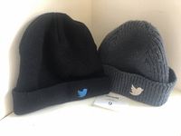 Pair of knit caps shown on a flat surface: one black with light blue Twitter emblem, one ribbed charcoal grey with white Twitter emblem.