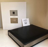 Black leatherette photo album with nickel-colored trim resting on shelf next to white box.