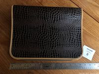 Top-down view of closed black binder with alligator embossed pattern, beige trim and a wooden ruler for scale.