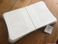 White Wii Balance Board accessory on wooden floor with auction tag
