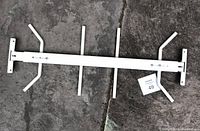 Full view of white steel adjustable fixed-mount window security bar placed on concrete floor showing mounting arms and vertical security rods.