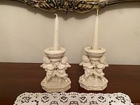 Full front view of both matching off-white vintage angel candle holders with taper candles inserted