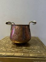 Front angled view of the antique copper bowl showing reflective copper surface and one ceramic handle on the right side with detailed blue hand painted pattern.