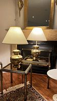Two brass table lamps on glass-top nesting tables in front of fireplace