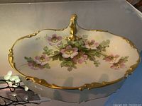 Angled top view of porcelain dish showing scalloped edges, gold trim, and pink rose flower decoration.