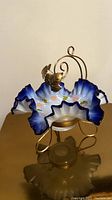 Side view of the antique Victorian style bride's basket showing brass scrollwork and applied leaf decoration with blue ruffled edge milk glass bowl hand-painted with flowers.