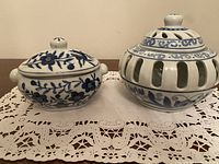 Two cobalt blue ceramic pieces on white lace doily, sugar bowl on left with floral design and lidded lantern on right with cutouts