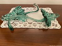Photo of two green art glass napkin holders on a lace doily, showing leaf shape and curved stems