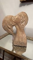 Front angled view of large beige stone sculpture showing two faces kissing, set on glass table.
