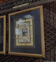 Full view of the large ornate gold frame with vintage art and attached brass museum light above.