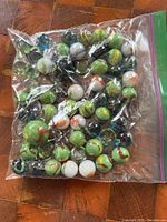 Plastic zip-top bag filled with approximately 48 vintage glass marbles of various colors and swirl patterns.