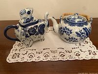 Front view of the two main ceramic teapots placed side by side on a lace table runner