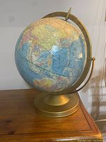 Side angle view of the 12-inch Cram’s Scope-O-Sphere globe showing Asia and Australia, mounted on gold-toned round base with semi-meridian ring