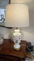 Full view of the antique milk glass table lamp with fabric drum lampshade on wooden table.