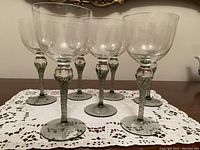 Front view of five mouth blown vintage art glass wine glasses with twisted stems on a lace doily.