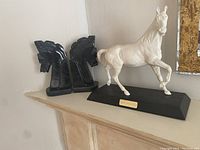 Photo showing the pair of black onyx horse head bookends and white horse figurine on black base labeled 'Spirit of the West'. The figurine is on the right and the bookends on the left.