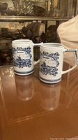 Photo showing two vintage Delft blue and white ceramic jugs with Heineken branding and Dutch windmill artwork.