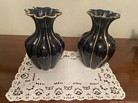 Pair of dark navy ceramic vases with gold hand-painted scalloped ridges and ruffled tops atop a white lace cloth, shown from front