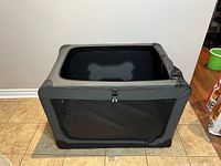 Photo of the closed foldable pet playpen, showing black fabric with grey trim and mesh side with bone design.