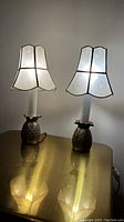 Pair of brass pineapple table lamps with illuminated Capiz shell shades on a reflective brass surface.