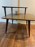 Close-up side view of one corner table showing wood grain and tapered legs with brass feet protectors.