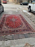 Full view of red Persian Kashan Garden rug laid on driveway showing overall pattern and condition
