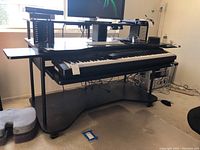 Wide angle side view of the adjustable height utility desk with pull-out keyboard tray containing a Yamaha digital piano keyboard, Dell monitor on stand, and side shelving visible.