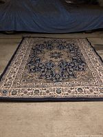 Top-down view of the 9x12 area rug showing the full blue and cream floral design with a prominent cream border and central medallion.