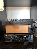Side view of black Musima MX602A audio mixer stacked on top of blue/black Pyle PTA4 stereo power amplifier with power cord coiled beside.