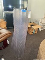 Clear plastic office chair mat, shown standing upright, illustrating thickness and texture.